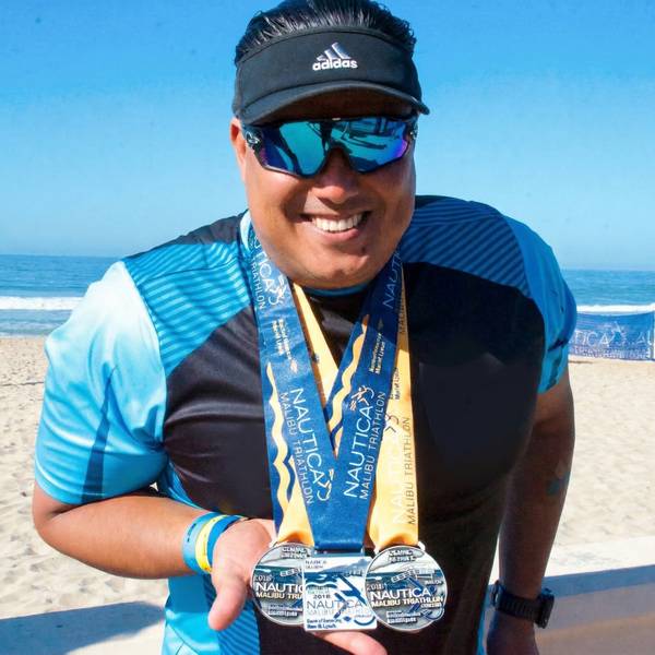 Marlon Duarte holding double Nautica Malibu Triathlon medals on the beach
