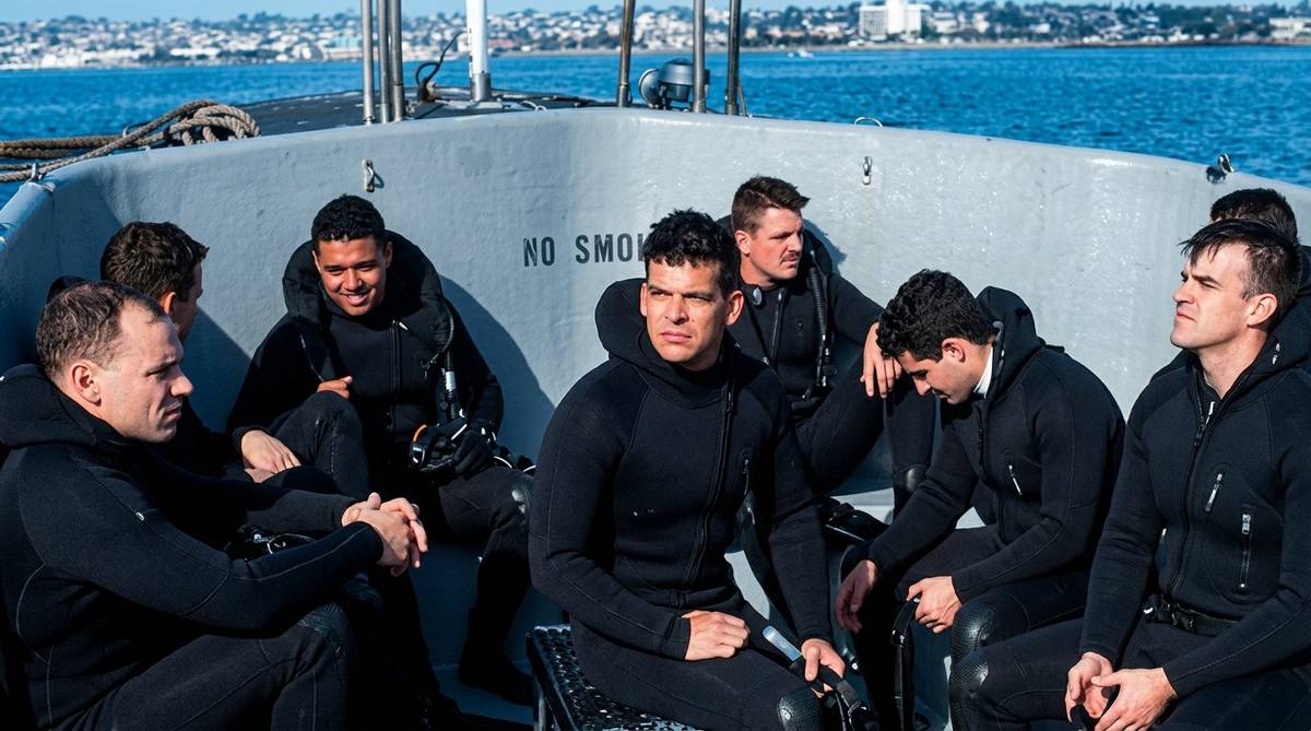 Navy SAR swimmers in wetsuits seated on military boat heading to final qualification test