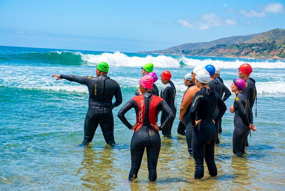 Coach Marlon leading ocean swim group at the beach, pointing toward the water