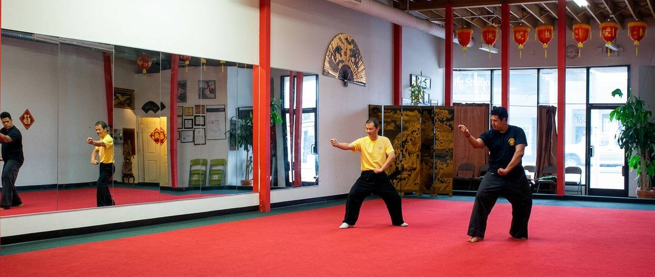 Marlon practicing Wu Shu forms with Grandmaster Hu in traditional dojo with red carpet and lanterns