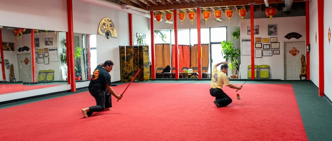 Marlon and Grandmaster Hu sparring with wooden swords in traditional dojo