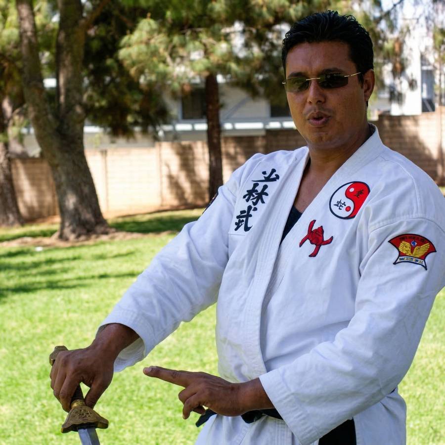Marlon in white gi with sword, sword fingers pose