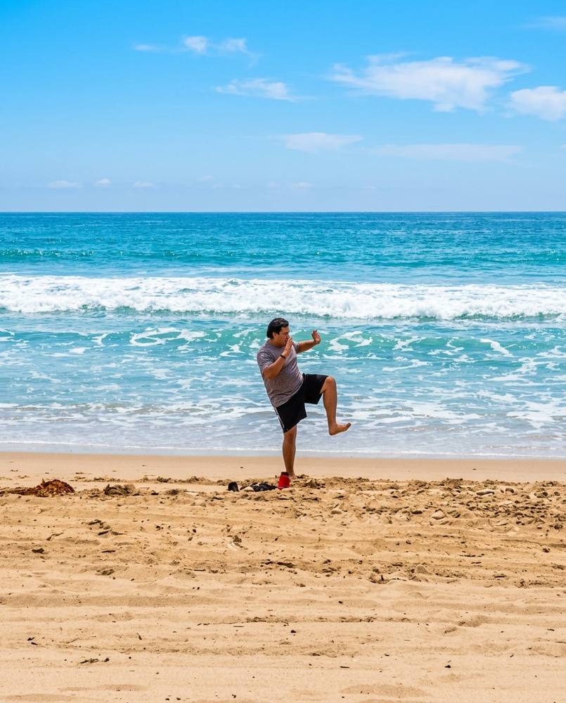 Marlon doing Tai Chi White Crane pose on the beach with ocean waves
